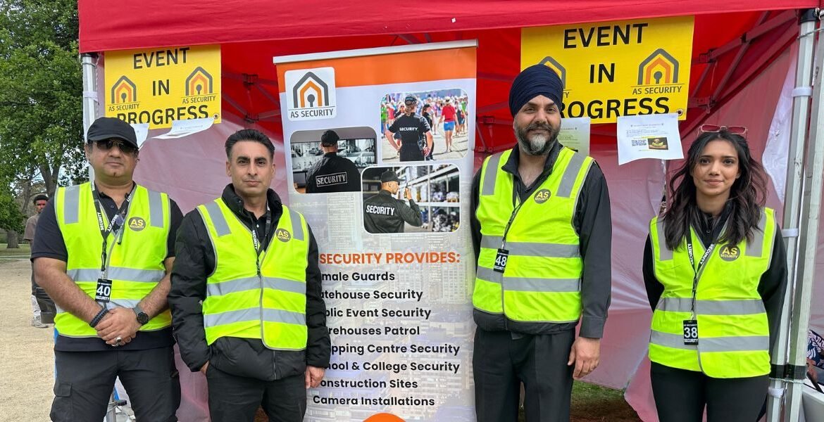 Event security team members in high-visibility vests standing in front of an AS Security banner, promoting services like public event security and crowd management, with an "Event in Progress" sign above.