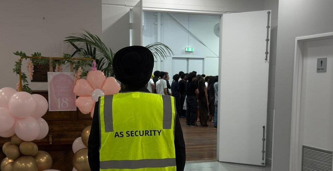 Concierge security officer in AS Security uniform overseeing a crowded event with decorative balloons and signage.
