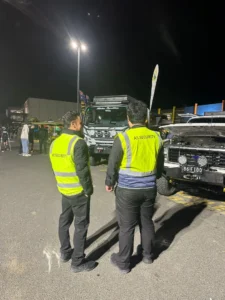 Security personnel in high-visibility vests monitoring vehicles at a car yard during nighttime, showcasing AS Security's commitment to safeguarding assets.