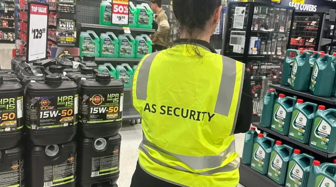 Person wearing a reflective vest with "AS SECURITY" text in a retail store aisle.